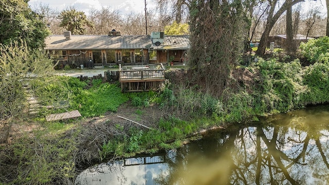 rear view of house with a deck with water view and a chimney