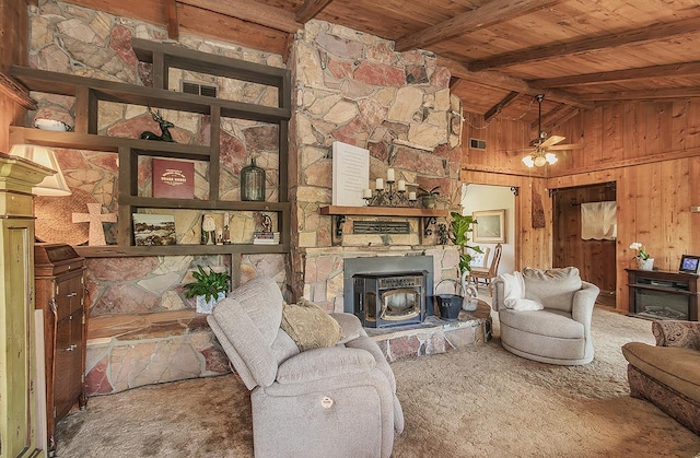 carpeted living room with beamed ceiling, wood walls, wooden ceiling, a wood stove, and a ceiling fan
