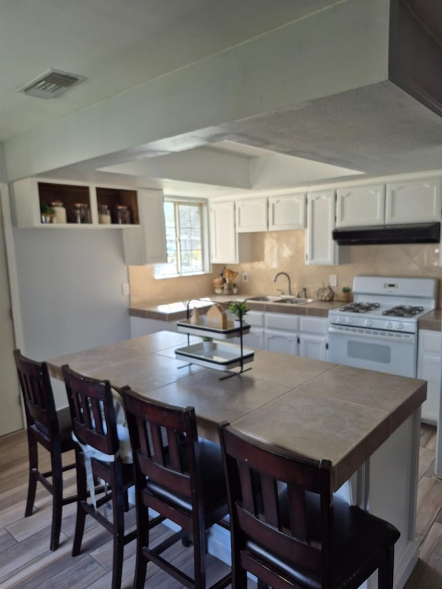 27261 Stanford Ave, Madera, CA 93637 - kitchen featuring white cabinets, visible vents, under cabinet range hood, tile countertops, and white gas stove