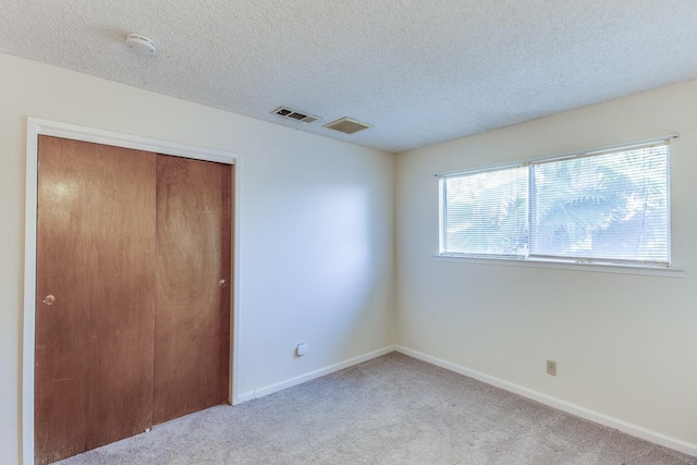 unfurnished bedroom with visible vents, carpet, a closet, and a textured ceiling