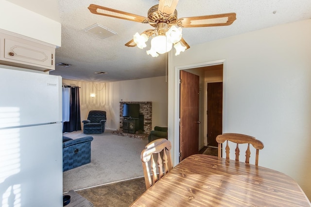 carpeted dining area with a textured ceiling, a wood stove, visible vents, and ceiling fan