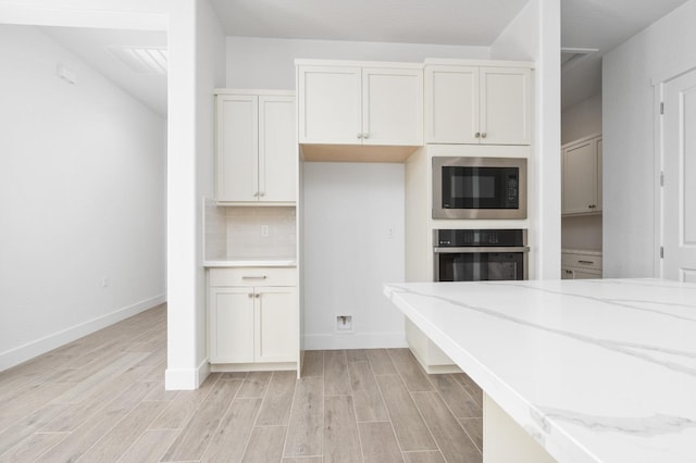 kitchen with light stone counters, built in microwave, oven, light wood-style flooring, and baseboards