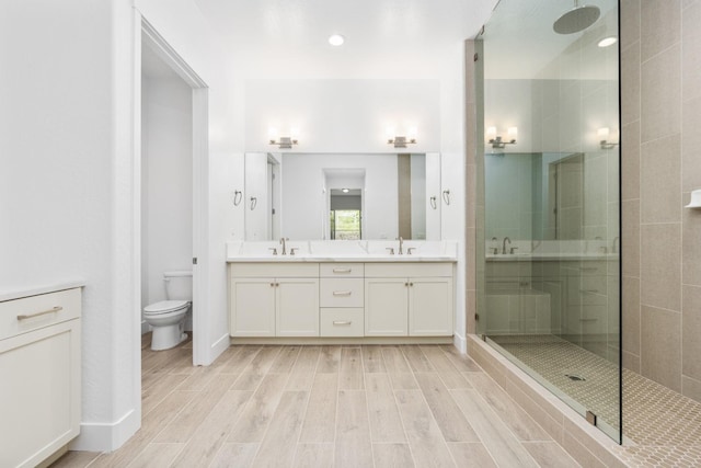 bathroom with a sink, double vanity, toilet, wood finished floors, and a shower stall
