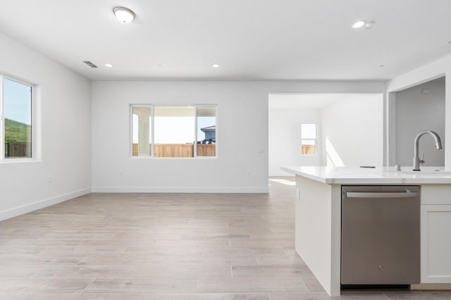 kitchen featuring stainless steel dishwasher, a sink, open floor plan, light wood-style floors, and light countertops