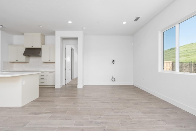 kitchen with under cabinet range hood, light countertops, visible vents, light wood-type flooring, and tasteful backsplash