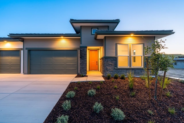 prairie-style house with an attached garage, driveway, and stone siding