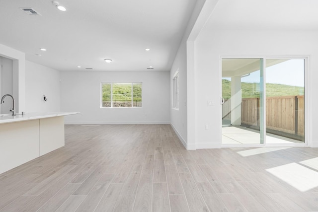 unfurnished living room featuring a sink, light wood-type flooring, baseboards, visible vents, and recessed lighting
