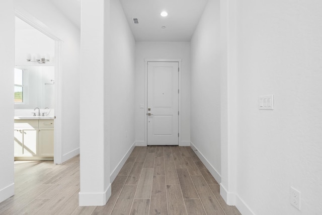 corridor with light wood-type flooring, baseboards, and a sink