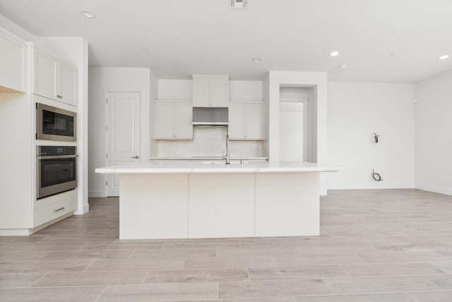 kitchen with stainless steel oven, decorative backsplash, built in microwave, and light wood-style floors