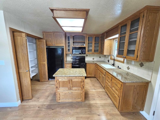 kitchen featuring a sink, light stone countertops, black appliances, and light wood finished floors