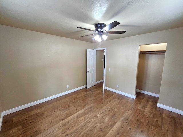 unfurnished bedroom with a closet, wood finished floors, a textured ceiling, baseboards, and ceiling fan