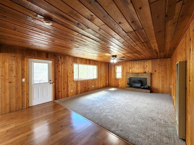 unfurnished living room with wood finished floors, a wood stove, wood ceiling, and wood walls