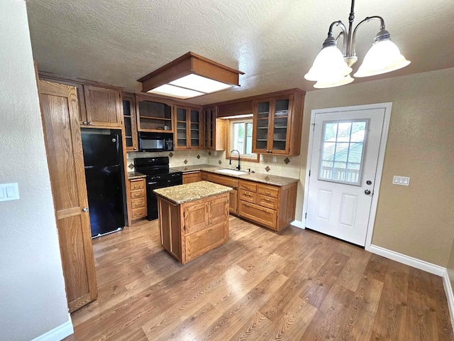 kitchen with a center island, a chandelier, a sink, light wood-style floors, and black appliances