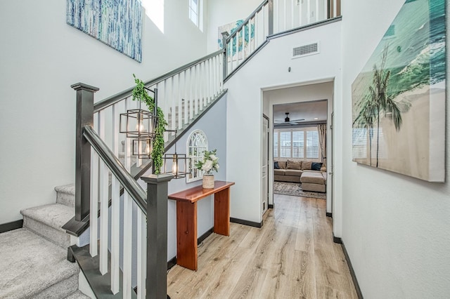 stairway with a high ceiling, baseboards, visible vents, and wood finished floors