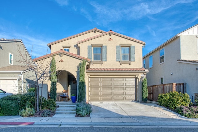 mediterranean / spanish home with a garage, a tiled roof, stucco siding, fence, and concrete driveway