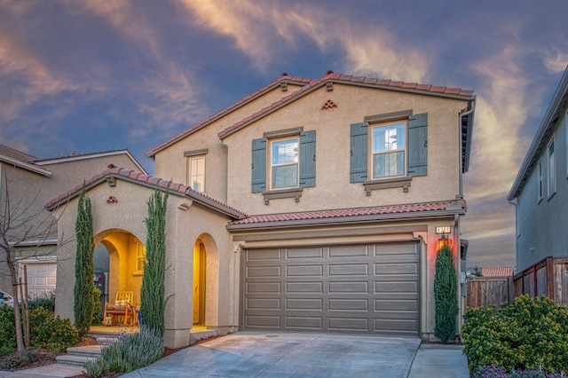 mediterranean / spanish house with a tiled roof, fence, an attached garage, stucco siding, and concrete driveway