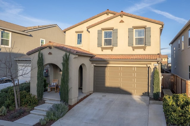 mediterranean / spanish-style home featuring an attached garage, a tiled roof, stucco siding, fence, and concrete driveway