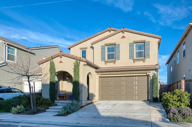 mediterranean / spanish home with an attached garage, a tiled roof, stucco siding, fence, and concrete driveway