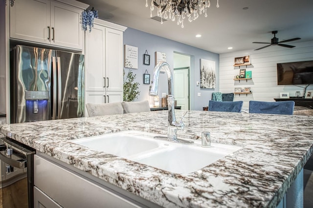 kitchen featuring a sink, light stone countertops, open floor plan, and stainless steel refrigerator with ice dispenser