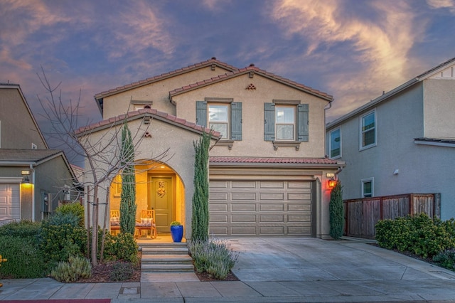 mediterranean / spanish-style house featuring fence, concrete driveway, a garage, stucco siding, and a tiled roof