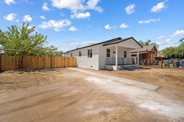 rear view of house featuring stucco siding, covered porch, and fence