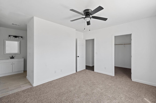 unfurnished bedroom featuring baseboards, light colored carpet, ensuite bath, and a spacious closet