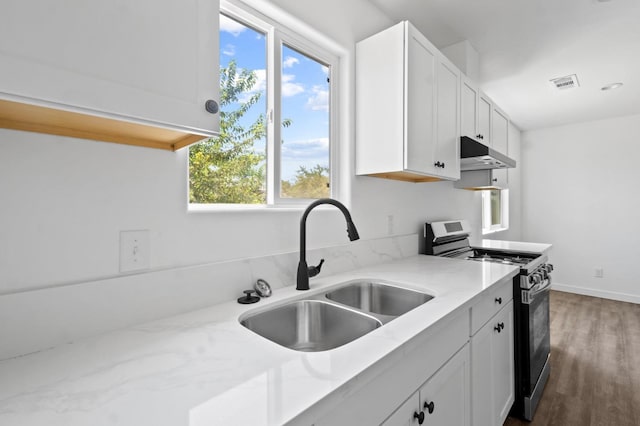 kitchen featuring visible vents, under cabinet range hood, gas range, white cabinets, and a sink