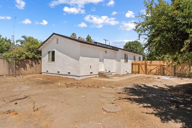 rear view of property with crawl space, stucco siding, a gate, and fence
