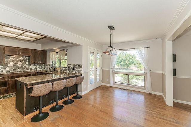 41371 Butte Way, Madera, CA 93636 - kitchen featuring dark brown cabinetry, tasteful backsplash, a breakfast bar, light wood finished floors, and crown molding