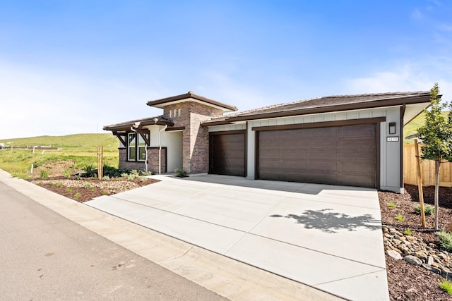 prairie-style house with concrete driveway, fence, a garage, stucco siding, and brick siding