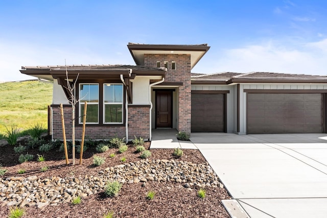 prairie-style house with concrete driveway, brick siding, and a garage