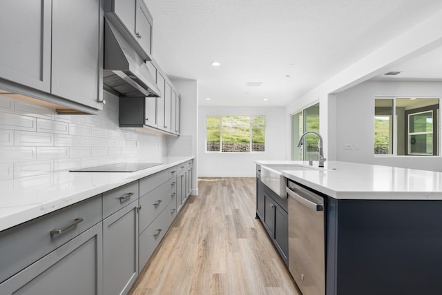 kitchen featuring a sink, light wood-style floors, gray cabinetry, dishwasher, and under cabinet range hood