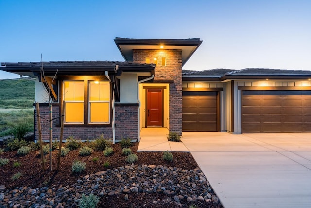 prairie-style home featuring an attached garage, stucco siding, brick siding, and concrete driveway