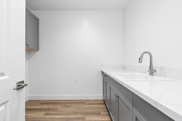 laundry room featuring baseboards, a sink, and light wood-style floors