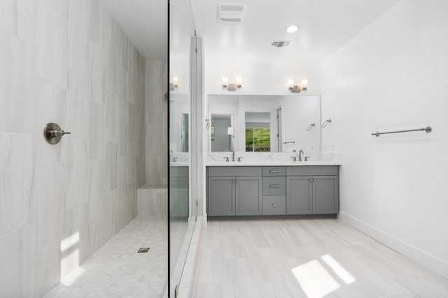 bathroom with a tile shower, a sink, visible vents, and double vanity