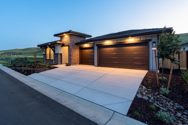 view of front of property featuring fence, a tiled roof, stucco siding, an attached garage, and driveway