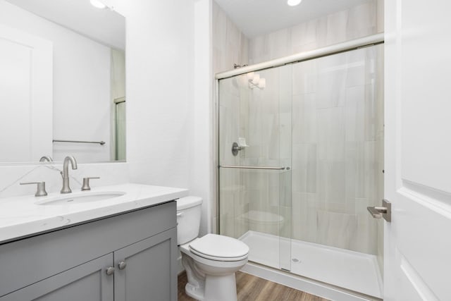 bathroom featuring a shower stall, toilet, vanity, and wood finished floors