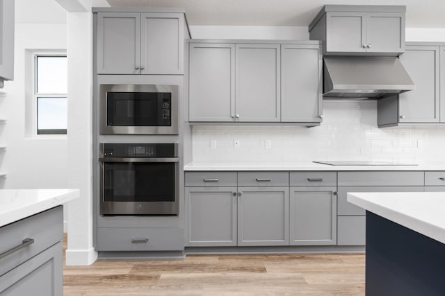 kitchen with oven, light countertops, wall chimney range hood, black electric stovetop, and gray cabinetry