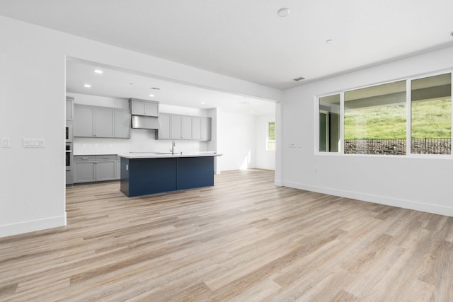 unfurnished living room with recessed lighting, light wood finished floors, baseboards, and a sink