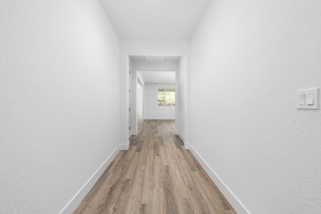 corridor featuring visible vents, baseboards, wood finished floors, and a textured wall