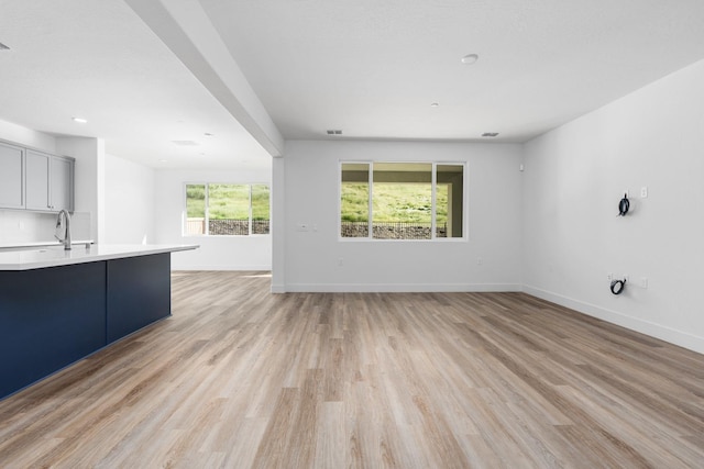 unfurnished living room with recessed lighting, baseboards, light wood-style floors, and a sink