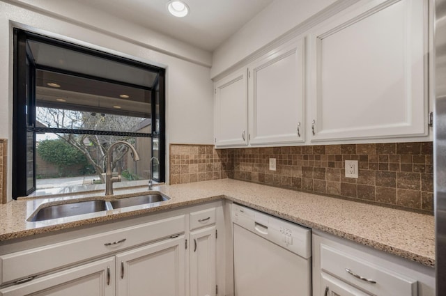 kitchen with white dishwasher, a sink, white cabinetry, backsplash, and light stone countertops