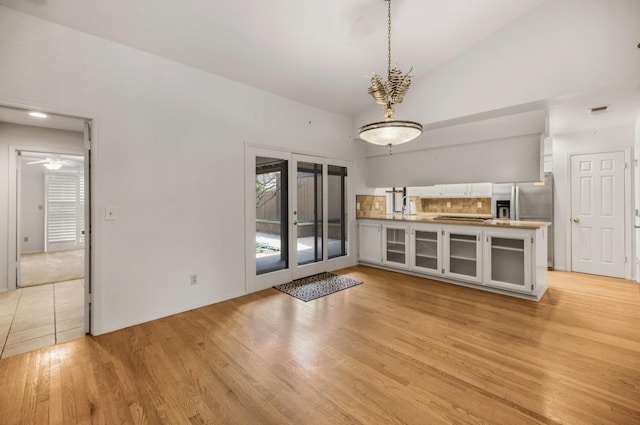 unfurnished dining area featuring light wood finished floors, a sink, and high vaulted ceiling
