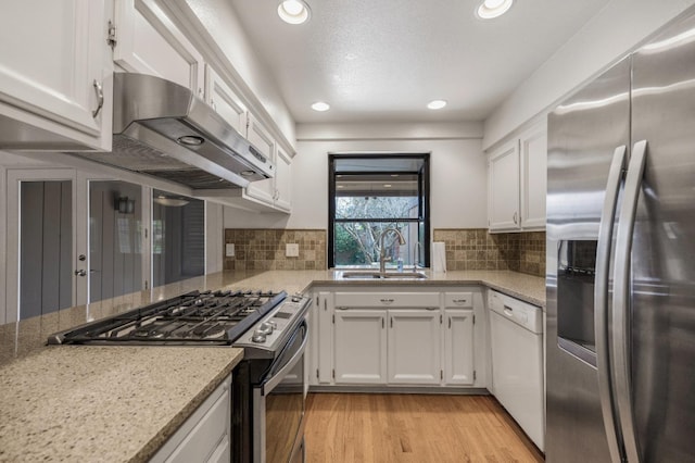 kitchen with appliances with stainless steel finishes, a sink, ventilation hood, white cabinetry, and recessed lighting