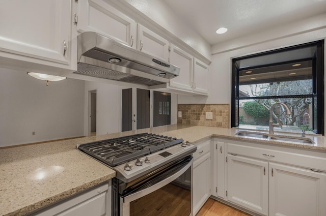 kitchen featuring stainless steel gas range, under cabinet range hood, a sink, and white cabinets
