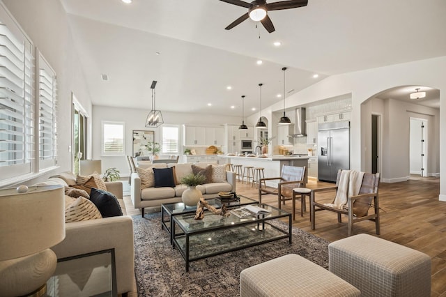 living area featuring vaulted ceiling, recessed lighting, wood finished floors, arched walkways, and a ceiling fan