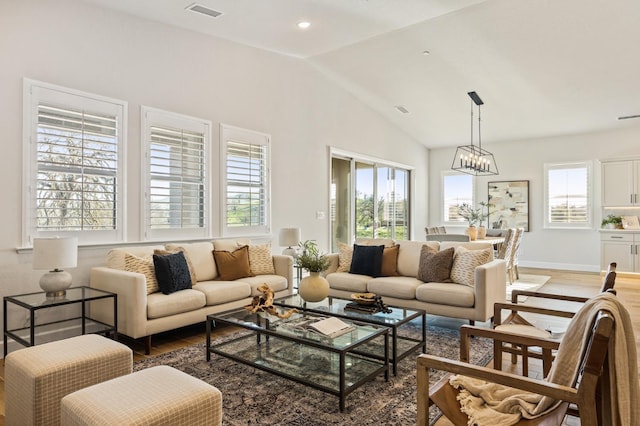 living area with visible vents, a chandelier, wood finished floors, and vaulted ceiling