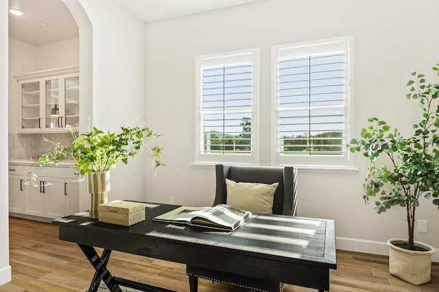 home office featuring light wood-style floors, arched walkways, and baseboards