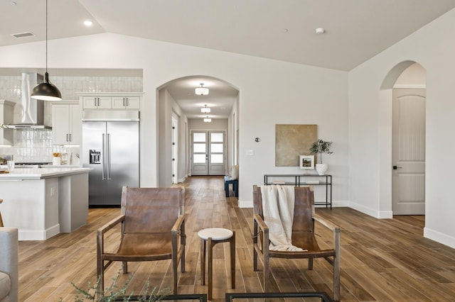 dining area featuring arched walkways, wood finished floors, and vaulted ceiling