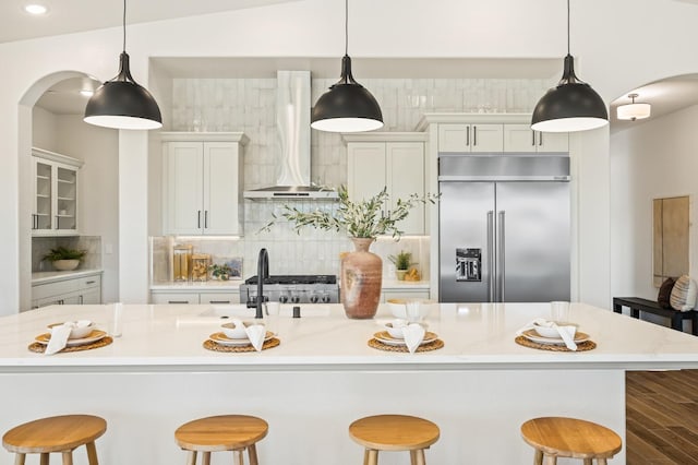 kitchen featuring tasteful backsplash, stainless steel built in refrigerator, light countertops, arched walkways, and wall chimney exhaust hood